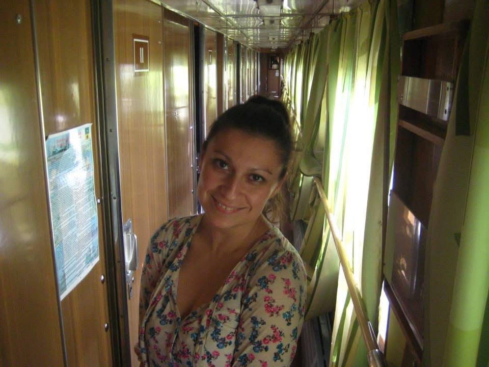 Photo of Olivia "Tina" Torres, standing in a hallway on a train. She is wearing a white top with pink and blue flowers.