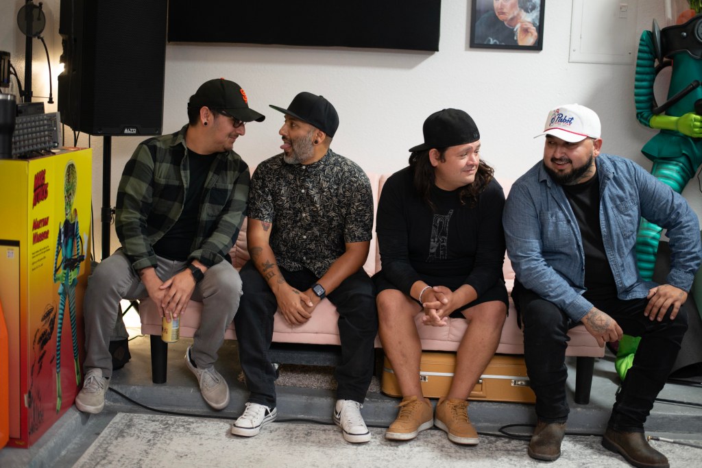 Photo of El Paso band Bloomwave. The band is sitting on a couch in a garage. Two members on the left are looking at each other, and on has his tongue out. Two members on the right side of the couch are smiling and looking at each other. Photo by Omar Mena.